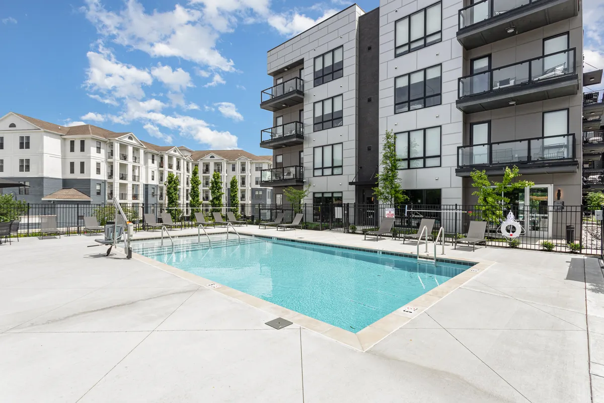 This image captures a vibrant exterior scene centered on the resort-style swimming pool, with balconies overlooking the water and surrounding residential buildings. The area is set up for leisure and socializing, with ample lounge space ideal for group gatherings.