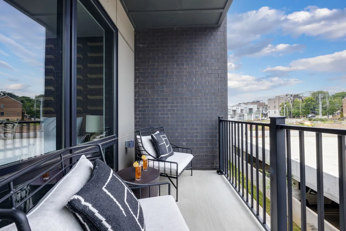 An outdoor balcony setup with comfortable seating, a table with a drink, and a sweeping city view. The mood is serene, suggesting an ideal spot for morning coffee or sunset relaxation while taking in the urban skyline.