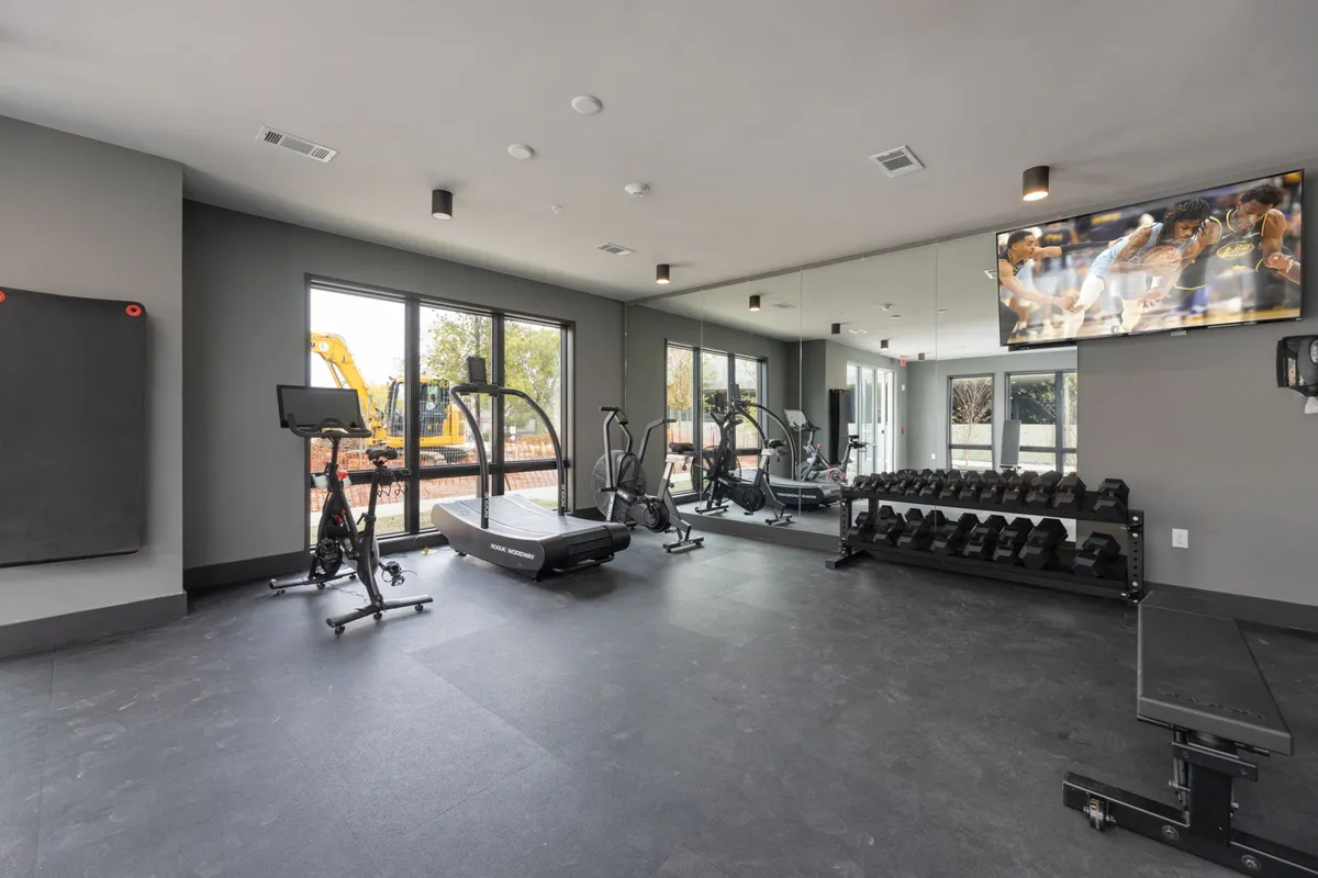 This interior shot showcases a well-equipped fitness center with treadmills, exercise bikes, free weights, large mirrors, and a mounted television. The room is bright, spacious, and modern, reflecting a state-of-the-art environment ideal for health-conscious guests.