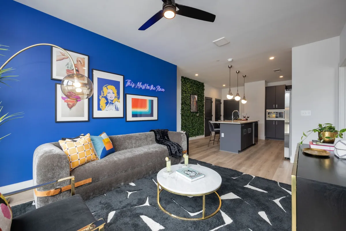 A stylish, sunlit living room featuring a lively blue accent wall adorned with playful artwork, a plush contemporary sofa, and a chic coffee table—perfect for gatherings or relaxing after a day exploring Nashville.