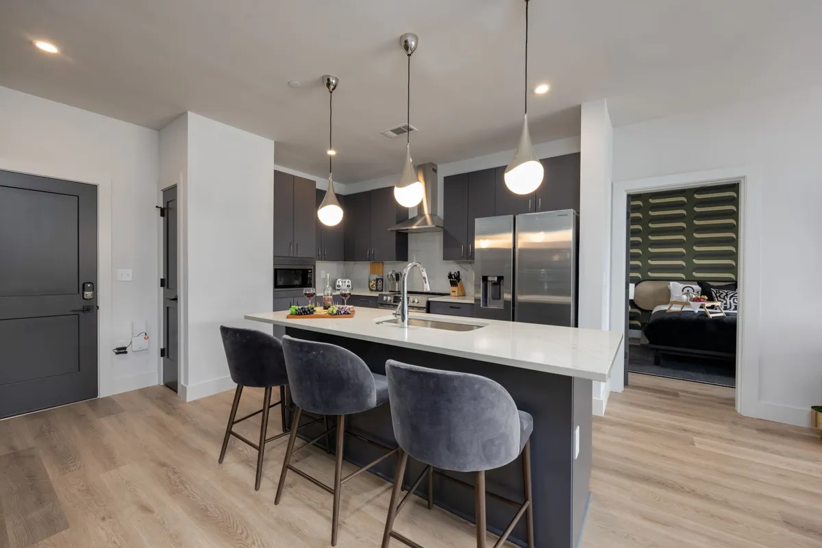 A stylish, modern kitchen with a central island surrounded by bar stools. Stainless steel appliances shine alongside neatly placed kitchen gadgets and a decorative fruit platter, creating a welcoming and upscale cooking and gathering space.